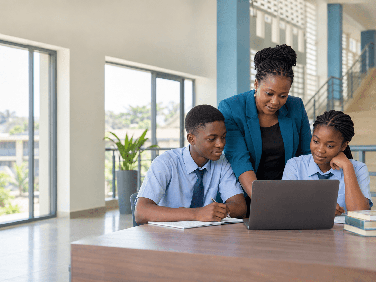 A teacher and two students in school uniform reviewing results together on a laptop